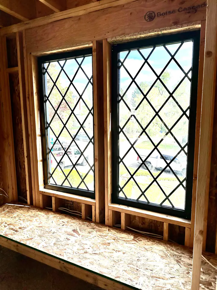 Close-up of diamond-pane window installation detail, precision shimming visible, new framing meets old structure