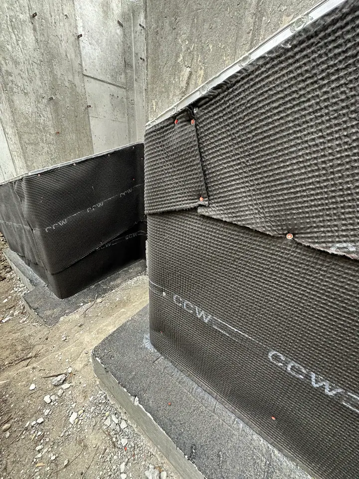 Close-up of CCW waterproofing membrane at foundation corner showing proper lapping and fastening technique