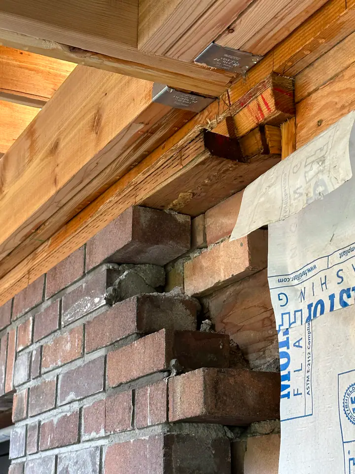 Close-up of new LVL beam connecting to existing brick wall with engineered metal joist hangers, critical structural connection point
