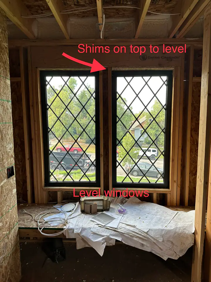 Annotated construction photo showing diamond-pane windows with red arrows pointing to shims on top to level, documenting precision work in an out-of-square structure