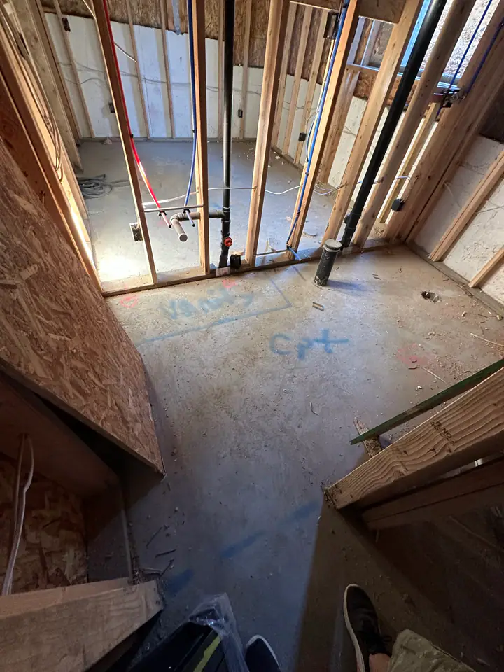 Looking down into basement showing PEX plumbing and ABS drain pipes, spray paint markings on concrete floor for layout coordination