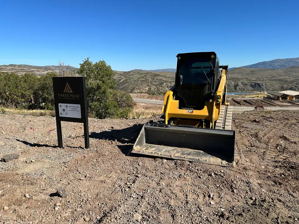 Close-up of Three Peak Construction sign, Dream, Design, Build, with equipment and reservoir visible