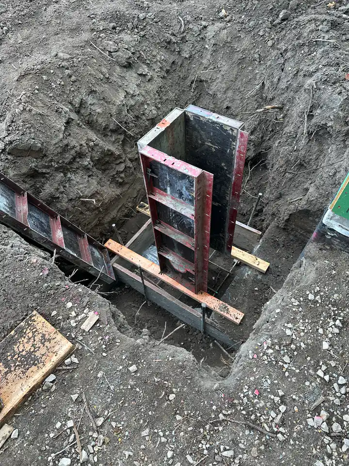 Steel foundation forms set in excavated trench, ready for concrete pour, the first permanent structure on the lot