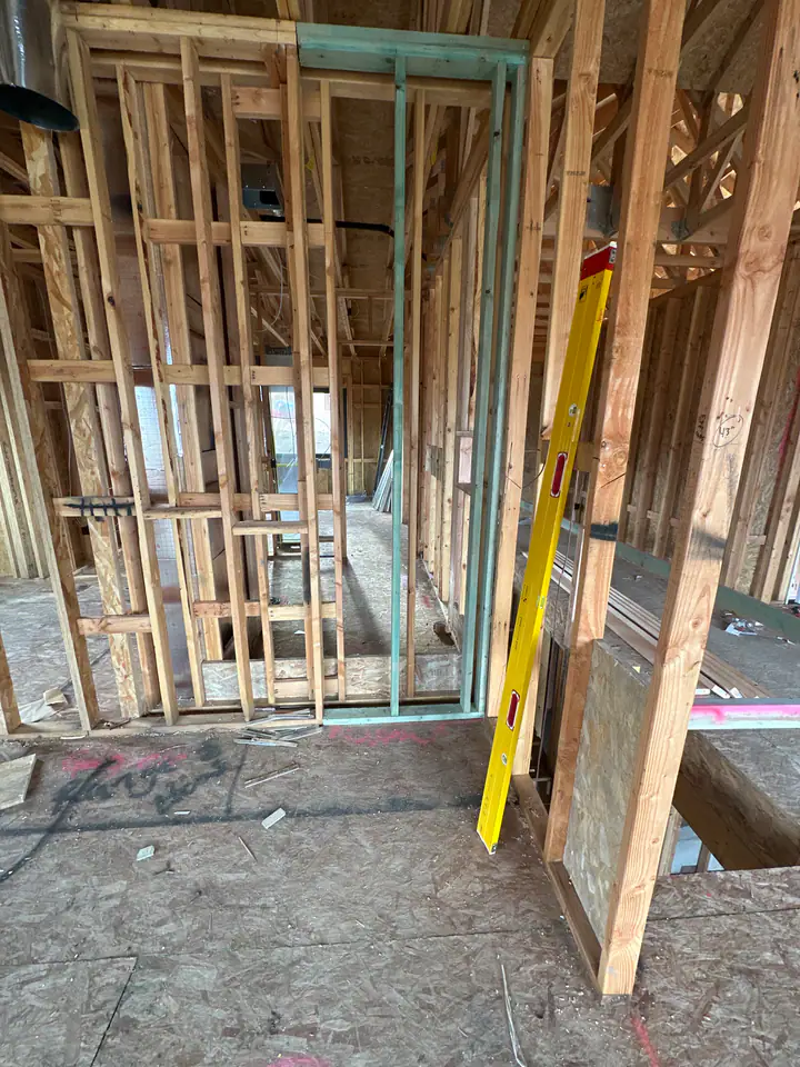 Interior framing detail, stud walls with yellow level, trusses overhead, OSB subfloor