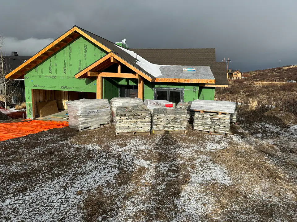 Front view of the home during framing, ZIP system sheathing, timber entry frame, roof trusses, stone pallets staged in foreground