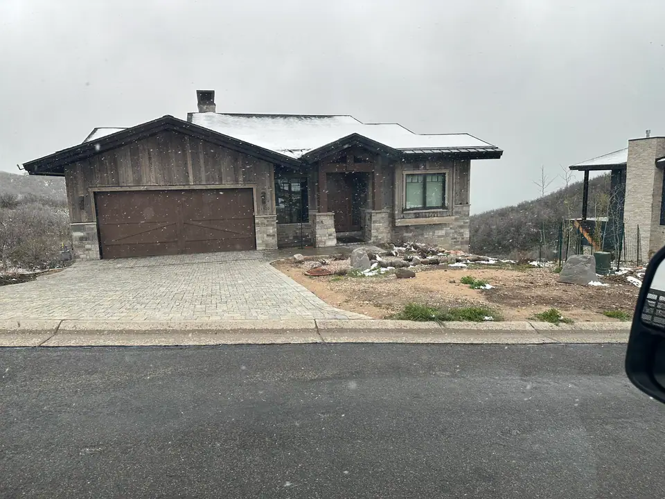 Near-complete exterior in snow, wood siding, stone columns, paver driveway, garage door installed