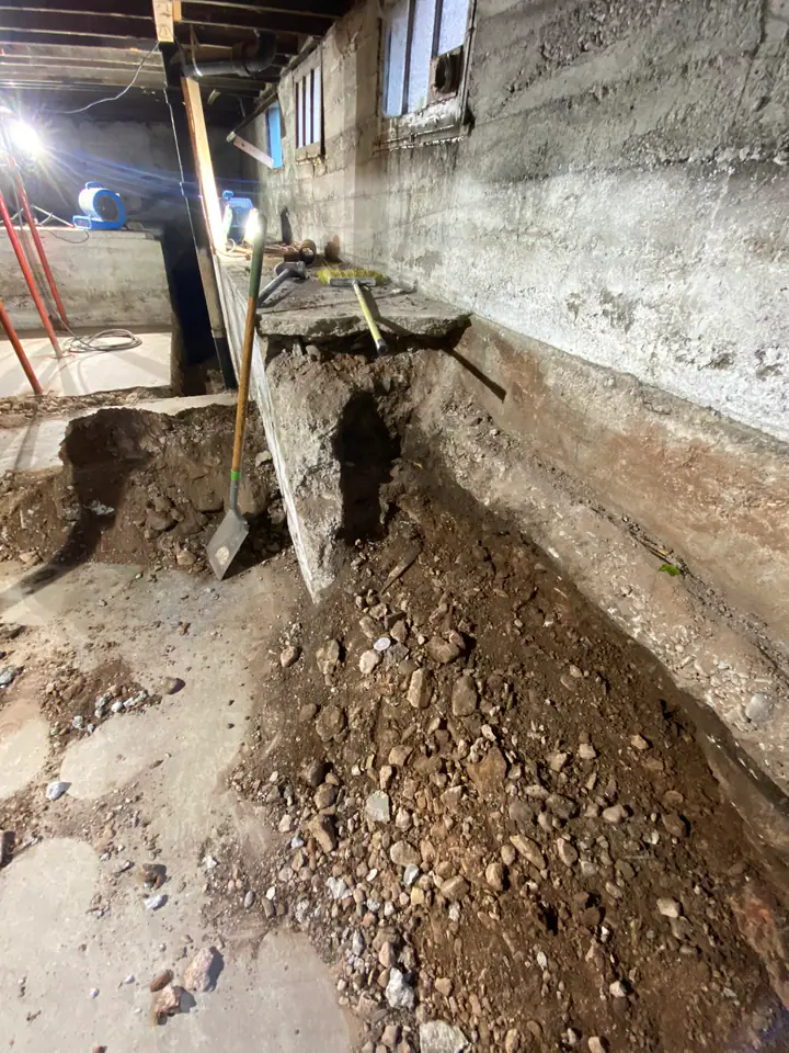 Long perimeter trench along foundation wall with air movers and support jacks, moisture management during structural repair