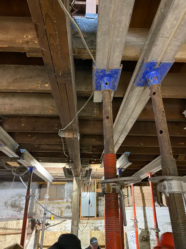 Temporary steel shoring jacks holding up the structure during foundation work, bare concrete and exposed framing