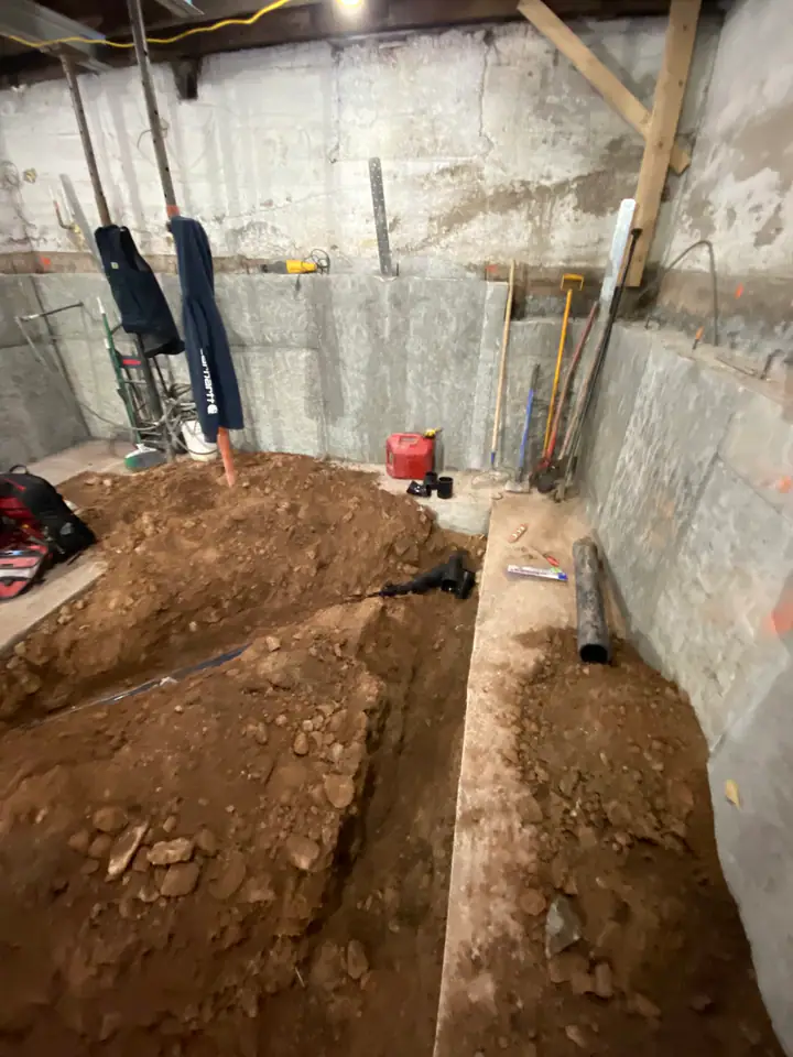 Basement excavation with dirt trenches dug for new footings and plumbing rough-in, ABS pipe visible alongside foundation work