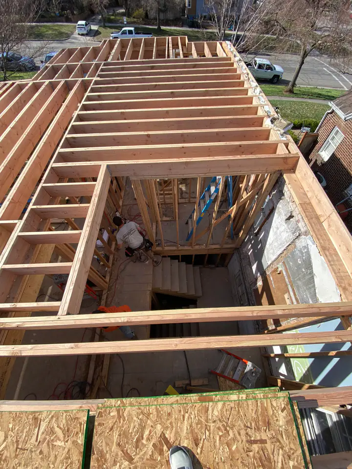 Aerial view looking down from roof level into the framed structure, stairwell, wall framing, original brick exterior visible