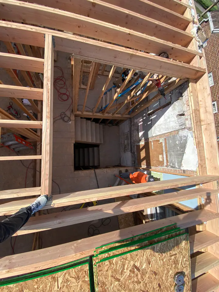Aerial view showing integration of old concrete block and brick structure with new dimensional lumber framing, workers in orange below
