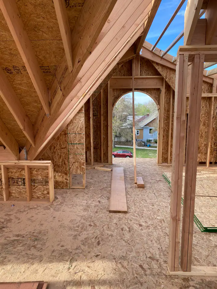 Interior of new upper level looking through arched window opening, roof rafters, OSB sheathing, blue sky visible