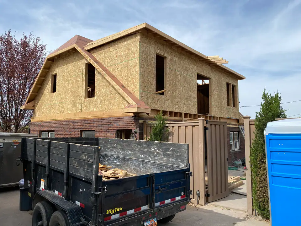 Complete exterior showing new second story addition on top of original brick first floor, multiple roof lines, window openings cut, full structural transformation