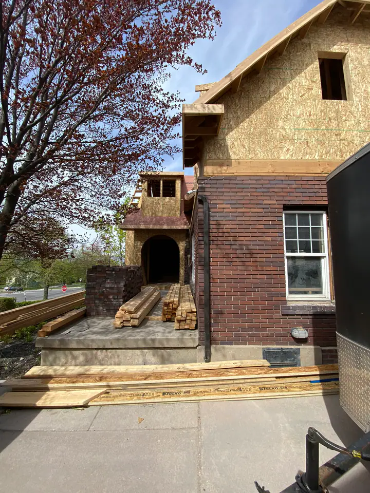 New tower entry addition with arched opening, original brick, lumber stacked on porch, old meets new architectural integration